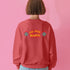 A Christmas sweatshirt featuring a playful design with a cartoon Baphomet goat character wearing a Santa hat. The design includes the text "All Hail Santa" above the goat, with pentagrams in flames on either side. The goat is depicted in a meditative pose, adding a humorous and irreverent twist to holiday attire.